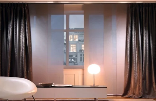 Dunkelbraune blickdichte Flächenvorhänge vor einem abendlichen Fenster in einem schwach beleuchteten Raum